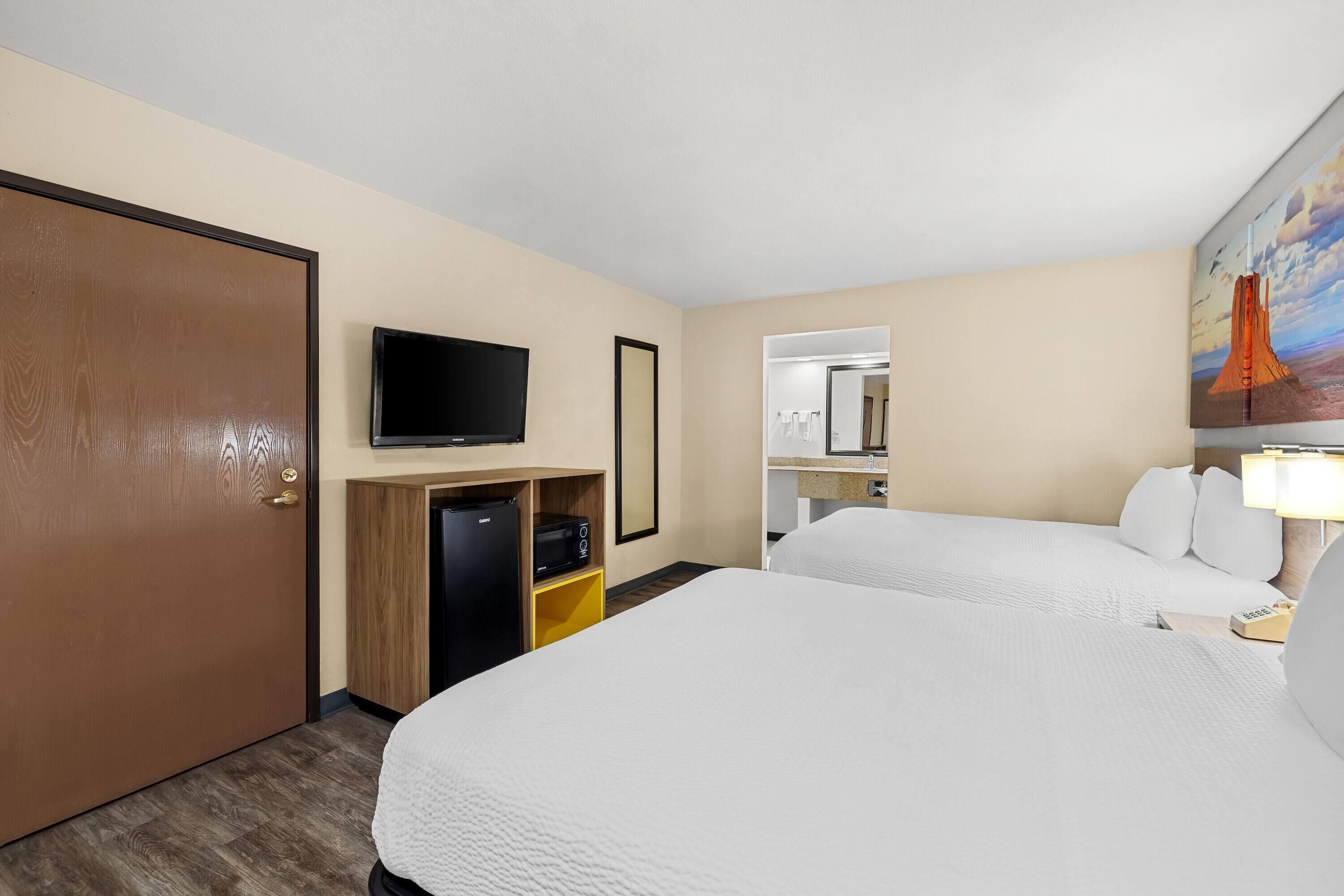 Una camera d'albergo con due letti, televisione, un minibar e un quadro appeso al muro.