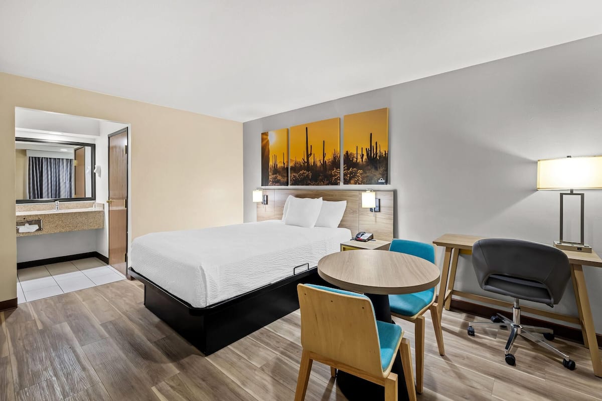 A hotel room with a bed, a round table, a chair, a desk, and a wall-mounted lamp.