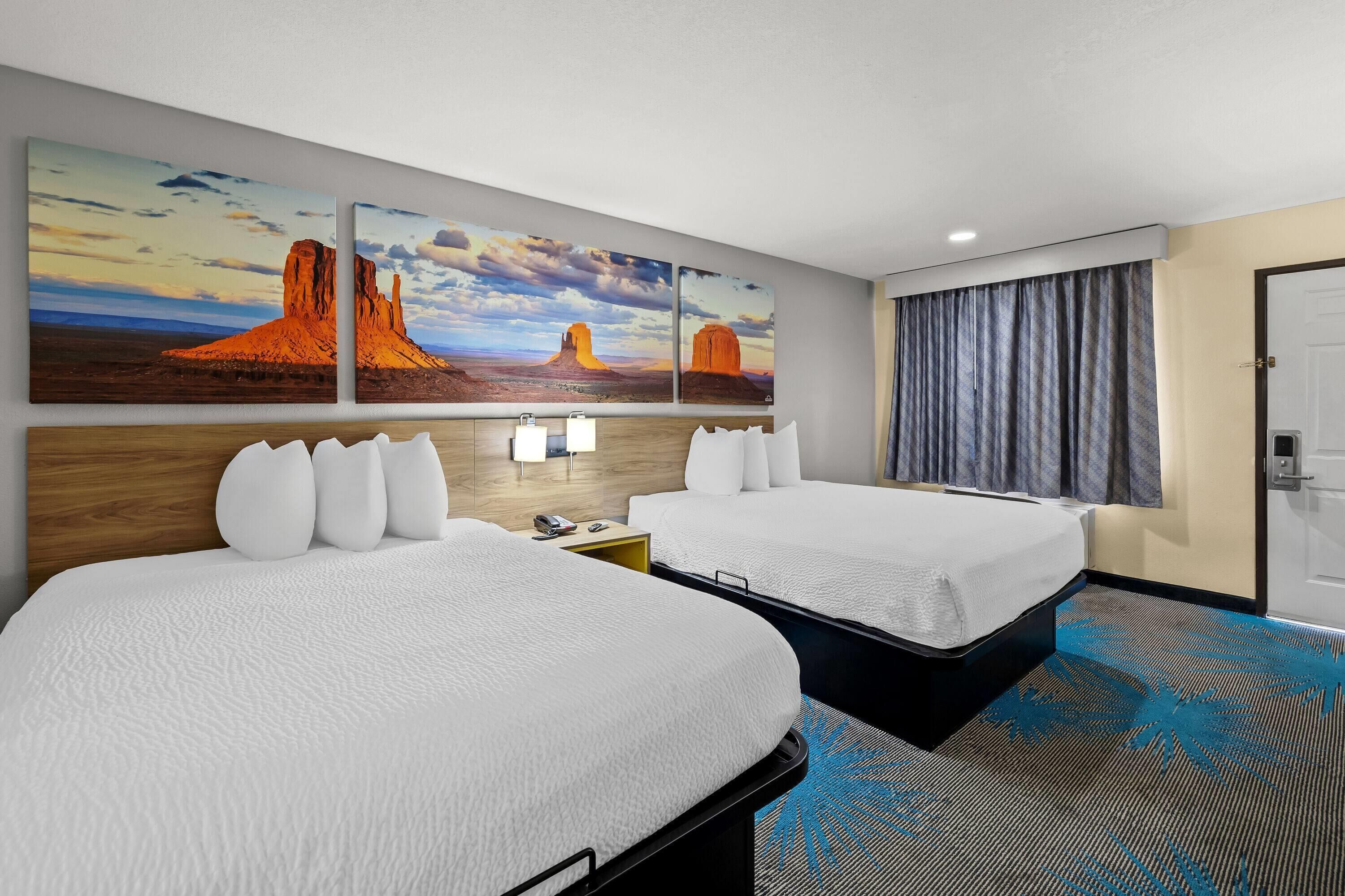 A hotel room with two beds, a large wall mural, a window with curtains, and a carpet with a blue pattern.