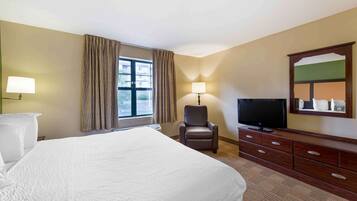 A hotel room with a large bed, a desk with a lamp, a television, and a dresser.