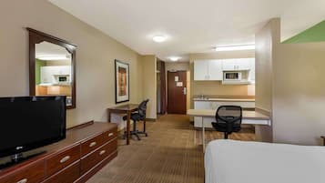 A hotel room with a bed, a desk, a chair, a TV, a dresser, and a kitchenette.