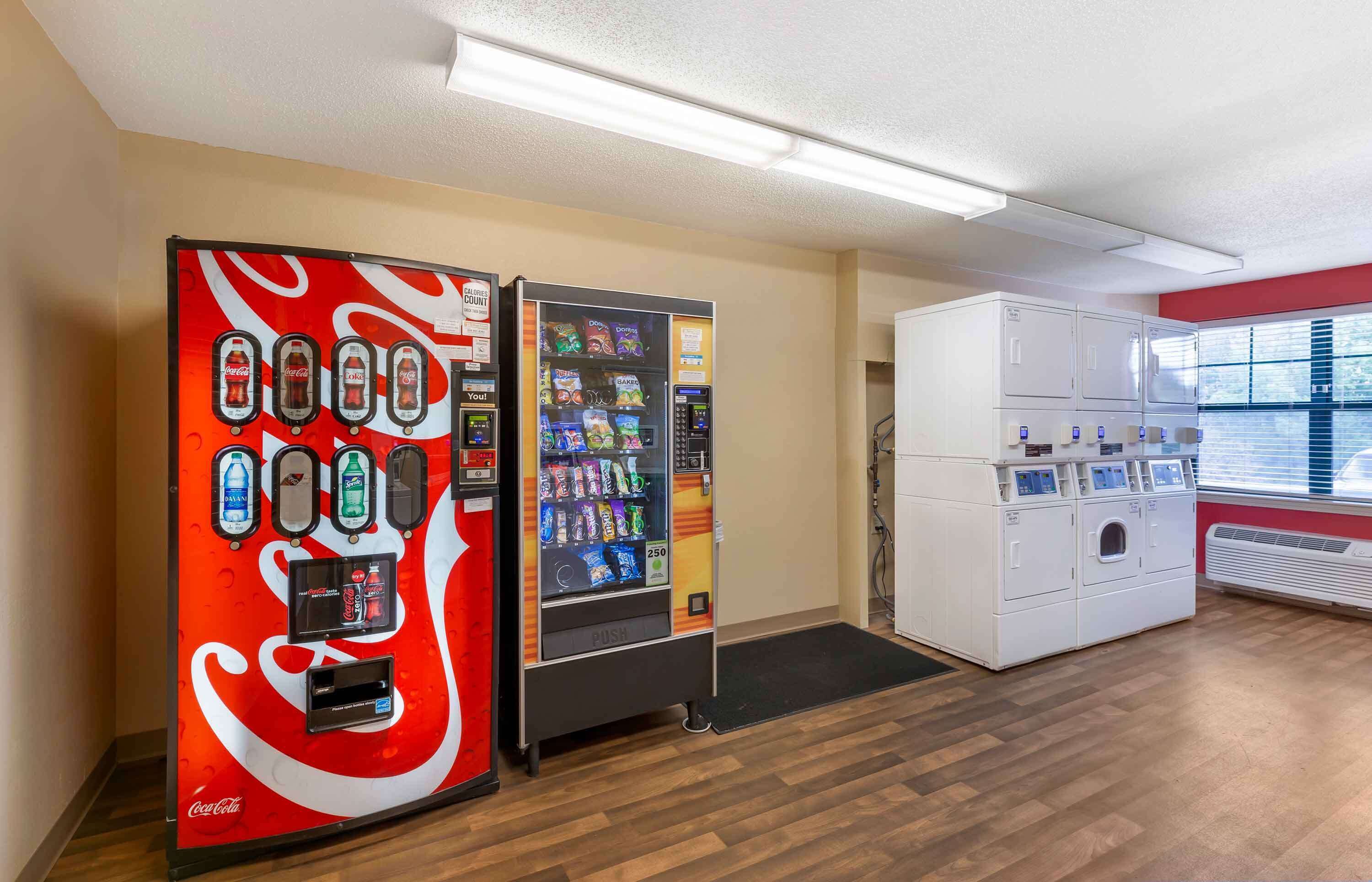 Un distributeur automatique de boissons, notamment de Coca-Cola, une machine à laver à commande par bouton-poussoir et une fenêtre avec des stores.