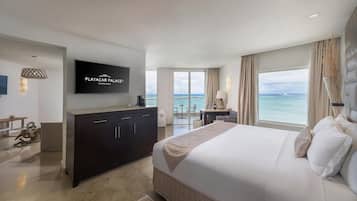 Quarto de hotel moderno com uma cama grande, televisão fixada na parede, escrivaninha com cadeira e vista para o oceano.