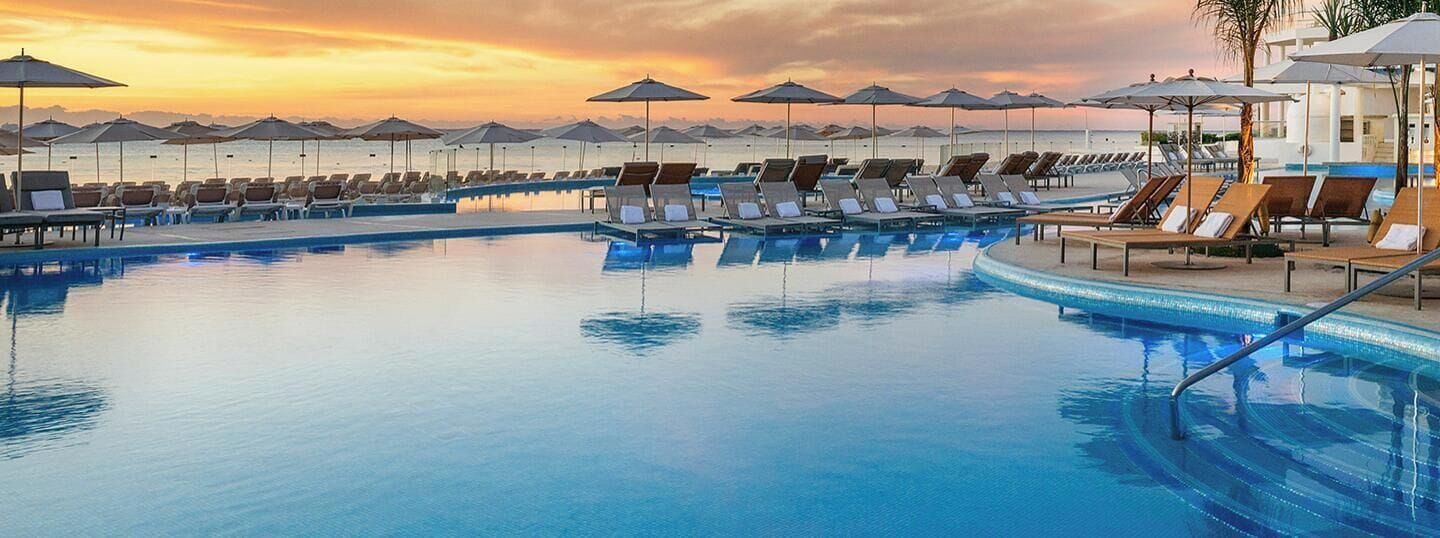 A pool area with lounge chairs and umbrellas, surrounded by a white building.