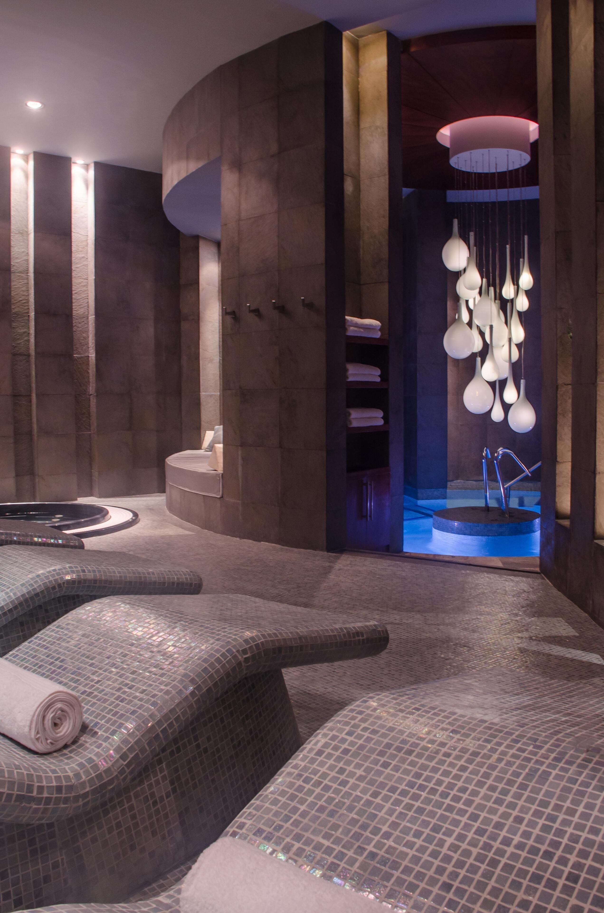 A modern spa area with a hot tub, seating areas, and a unique light fixture.