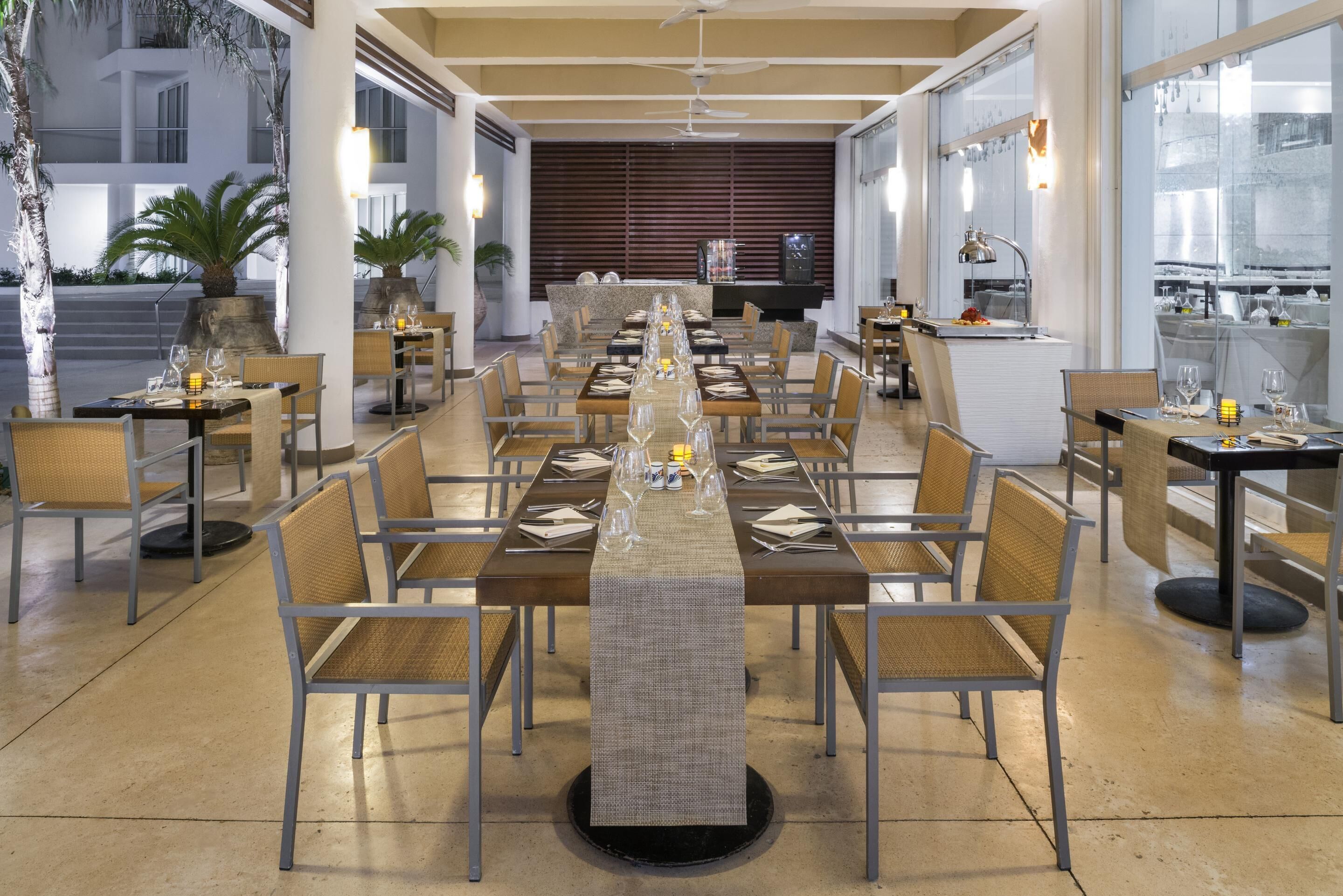A long dining table set with chairs, a central decorative piece, and a view of the building's exterior.