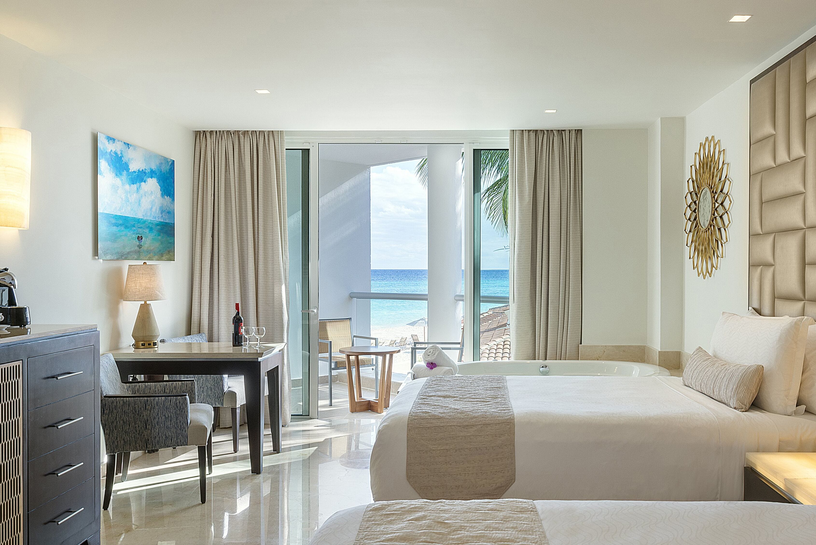 A hotel room with a large bed, a desk with a chair, a table, and a view of the beach.