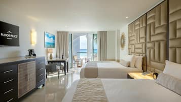 A hotel room with two beds, a TV, a desk, and a view of the ocean.