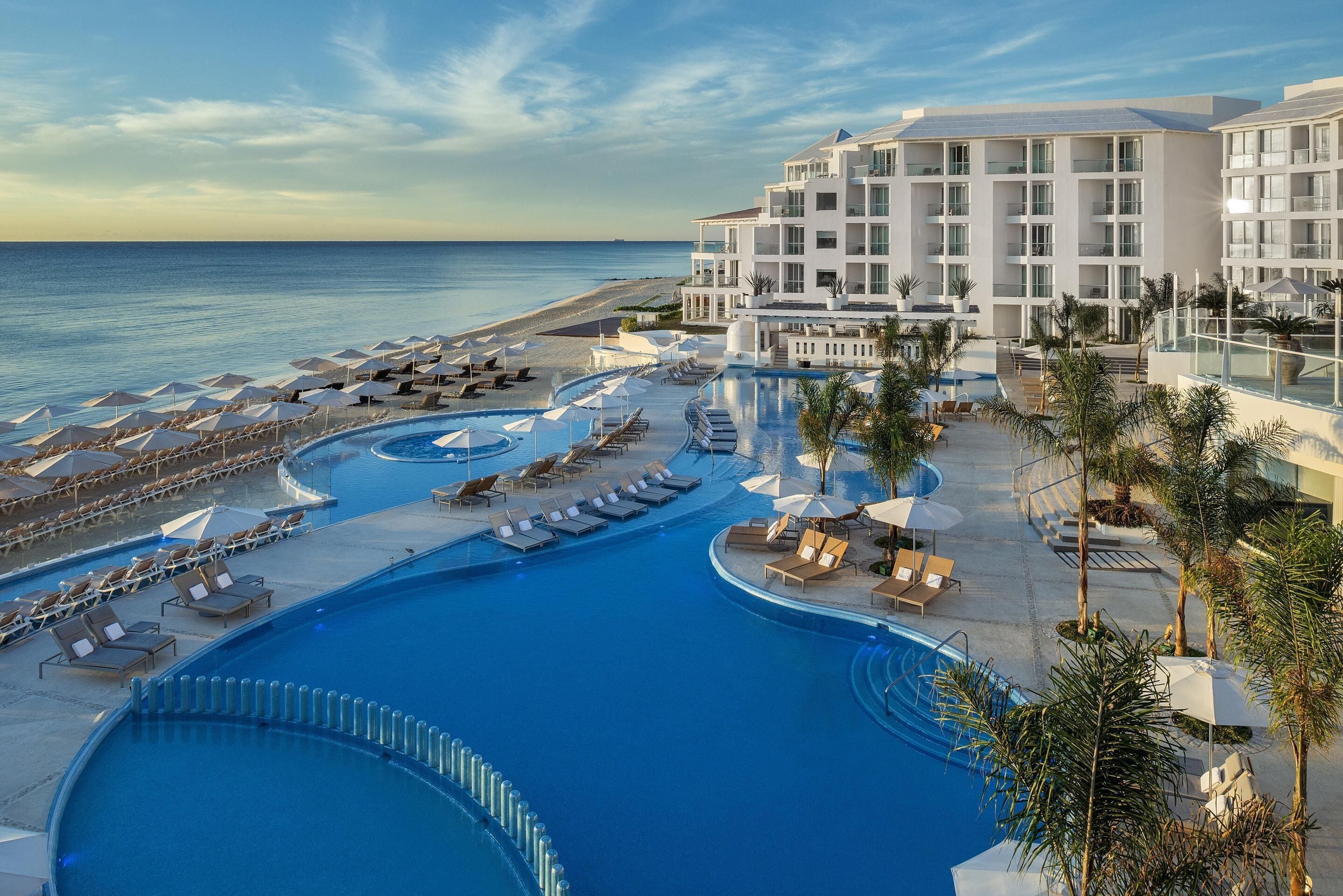 A resort with a large pool, sun loungers, umbrellas, and a beach view.