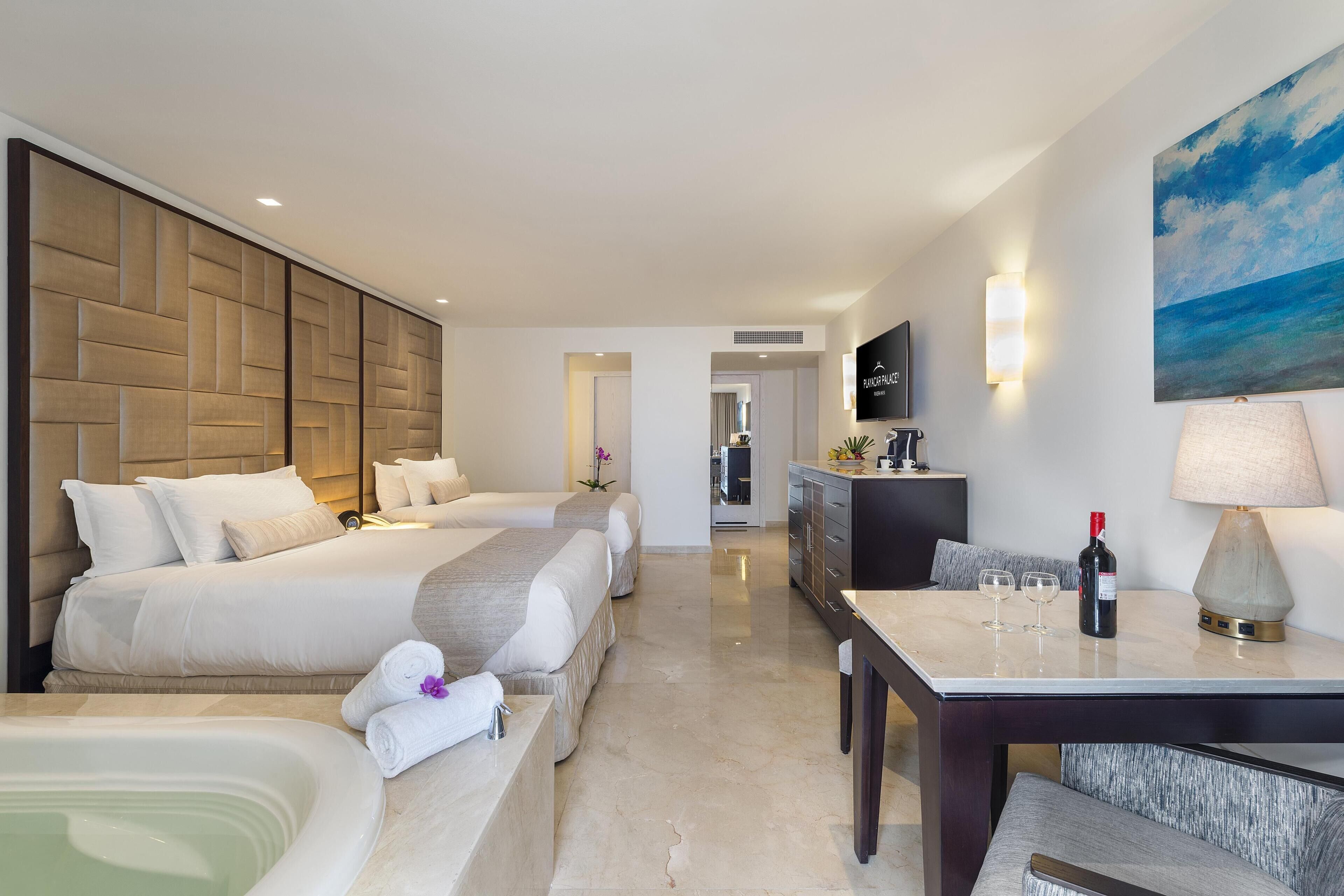 A hotel room with two beds, a sitting area with a table, a large painting, and a TV on the wall.