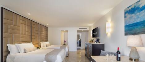 Habitación de hotel con dos camas, un área de descanso con mesa, un cuadro grande y un televisor en la pared.