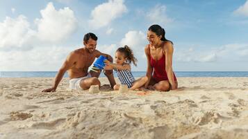 Una familia de tres personas en una playa arenosa, con un cielo despejado y el océano al fondo.