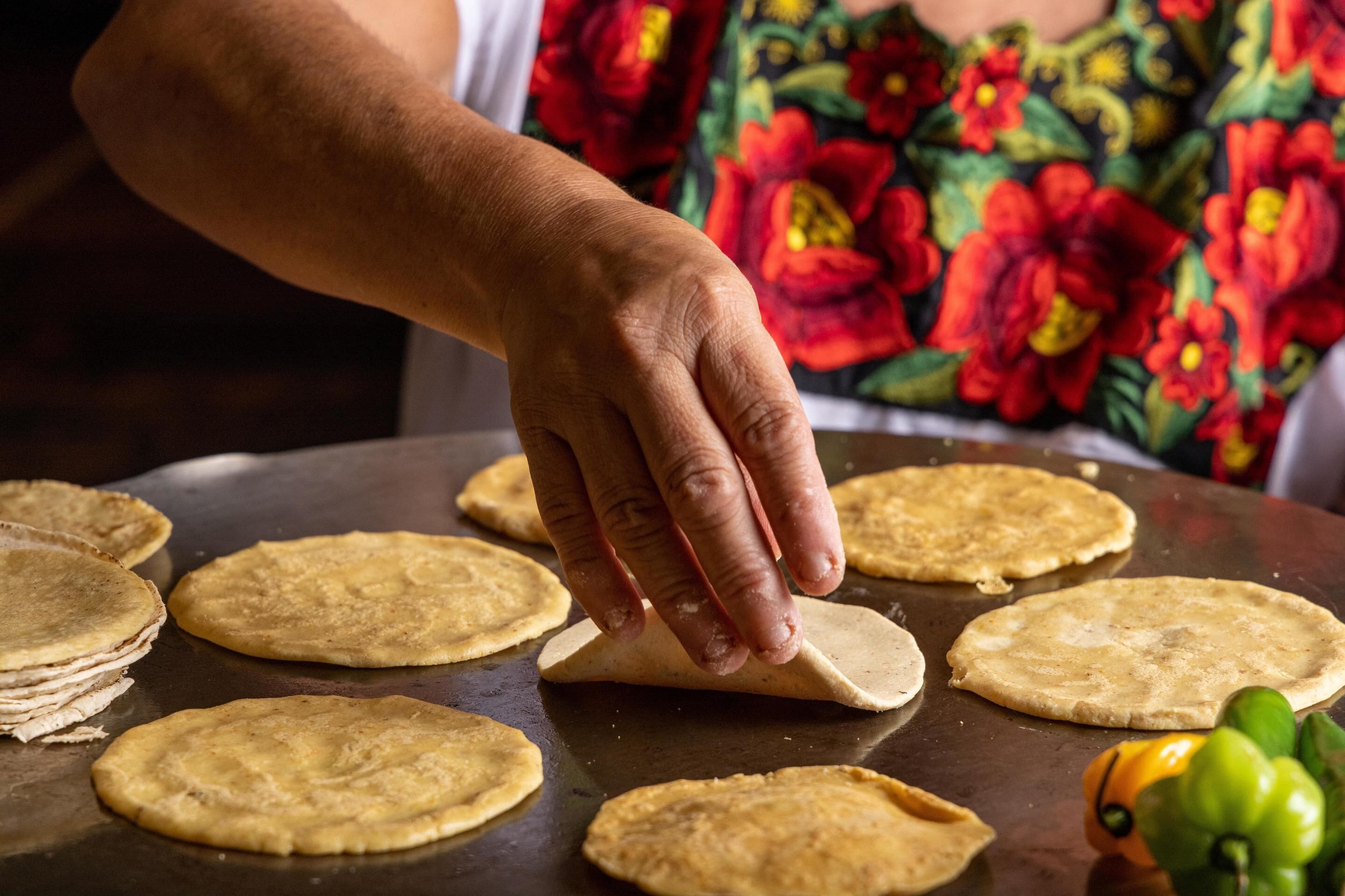 Uma pessoa colocando um pão achatado sobre uma superfície de metal, com vários outros pães achatados ao redor.