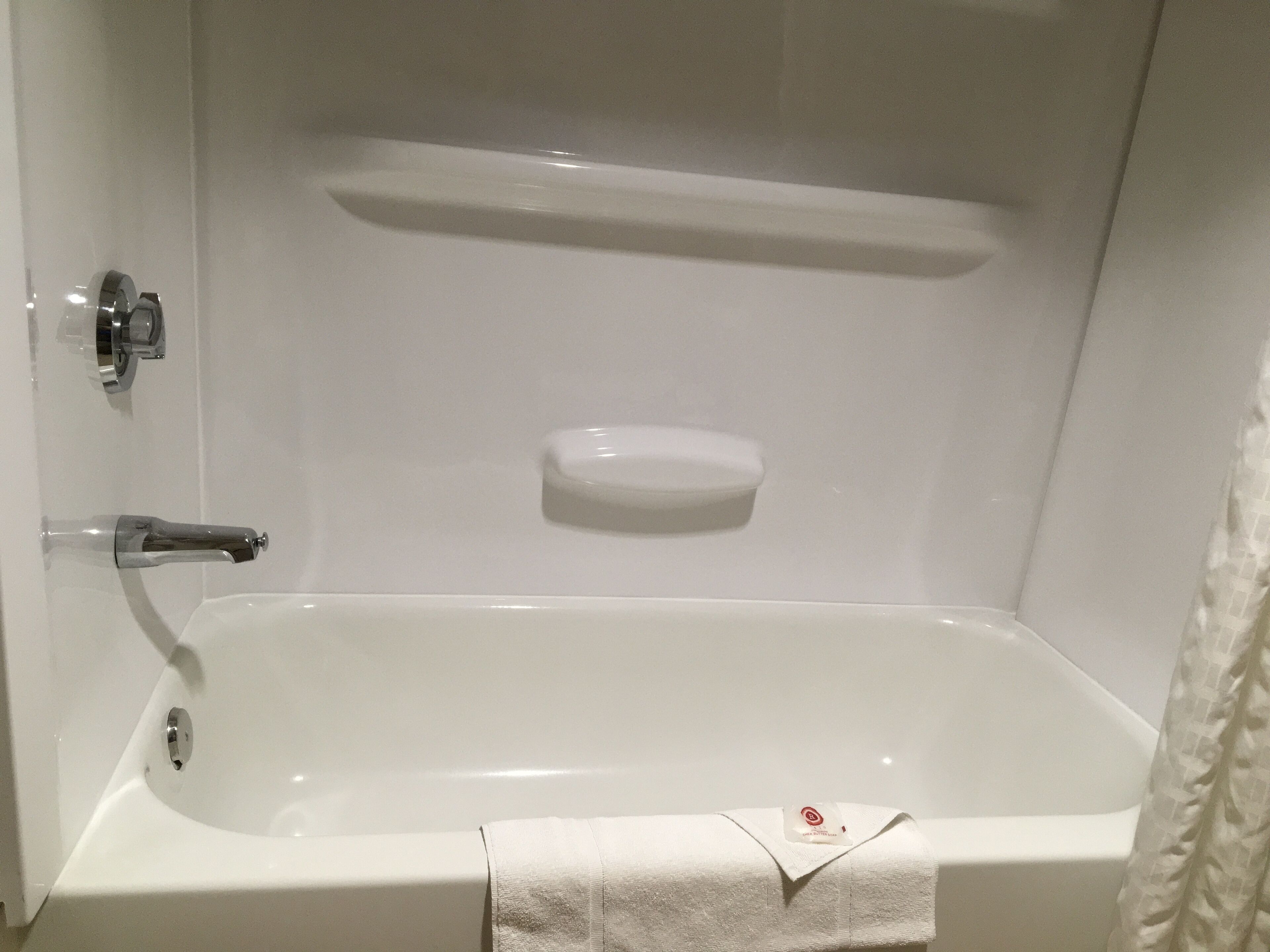 A white bathtub with a soap dish and a towel.