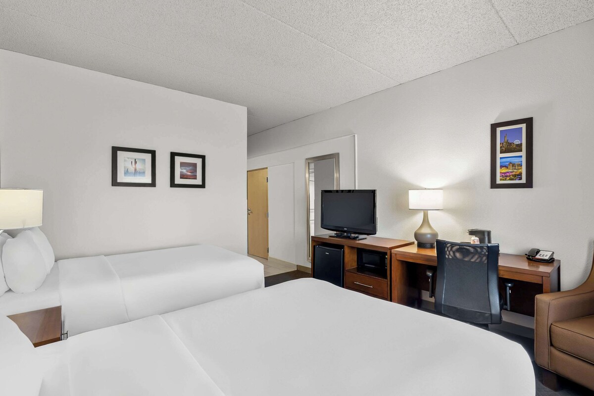 A hotel room with two beds, a desk with a television, a chair, and a lamp.