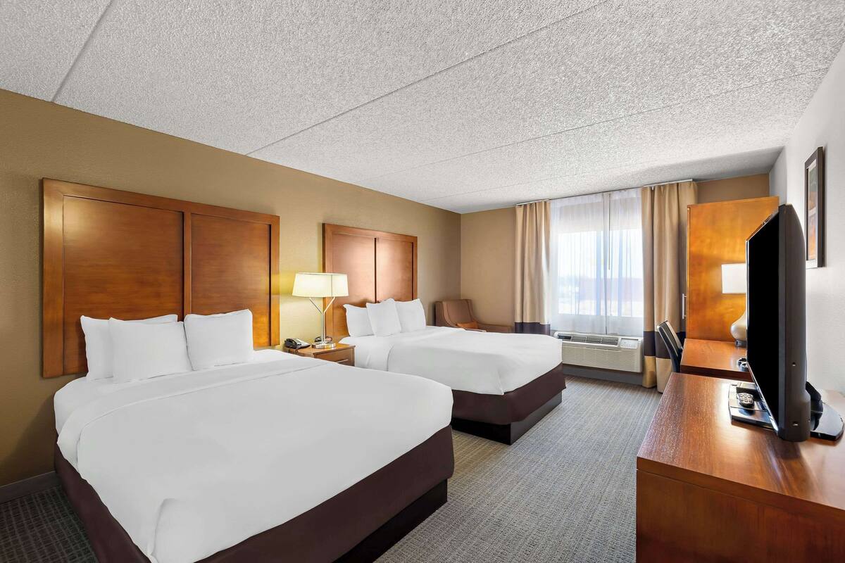 A hotel room with two beds, a desk, a television, and a window with curtains.
