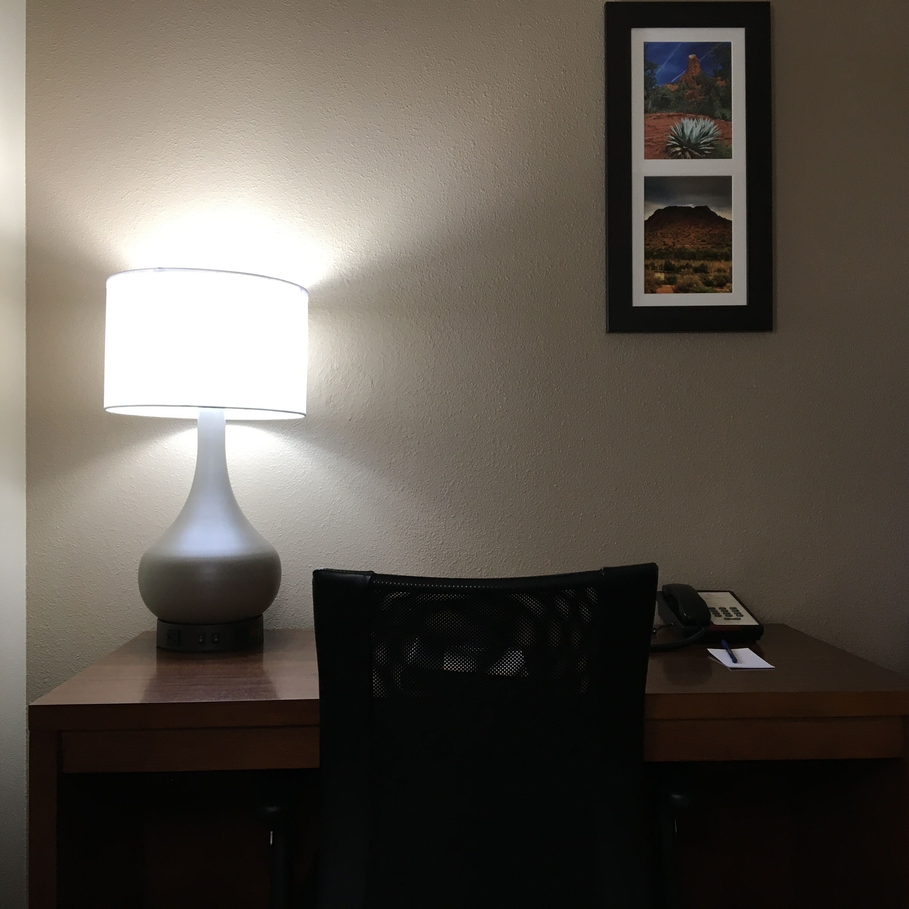 A desk with a lamp, a chair, and a framed picture on the wall.