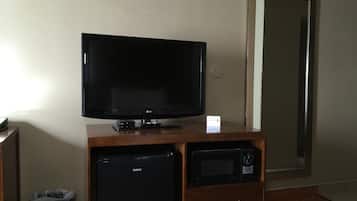 Une chambre d’hôtel équipée d’un téléviseur à écran plat posé sur un meuble en bois, d’un petit réfrigérateur noir, d’un four à micro-ondes et d’une poubelle de recyclage bleue.