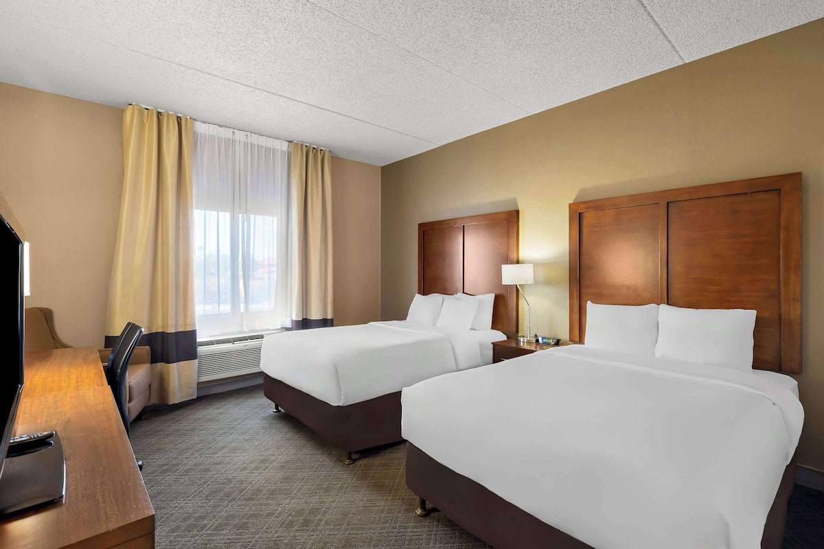 A hotel room with two beds, a desk, and a TV.