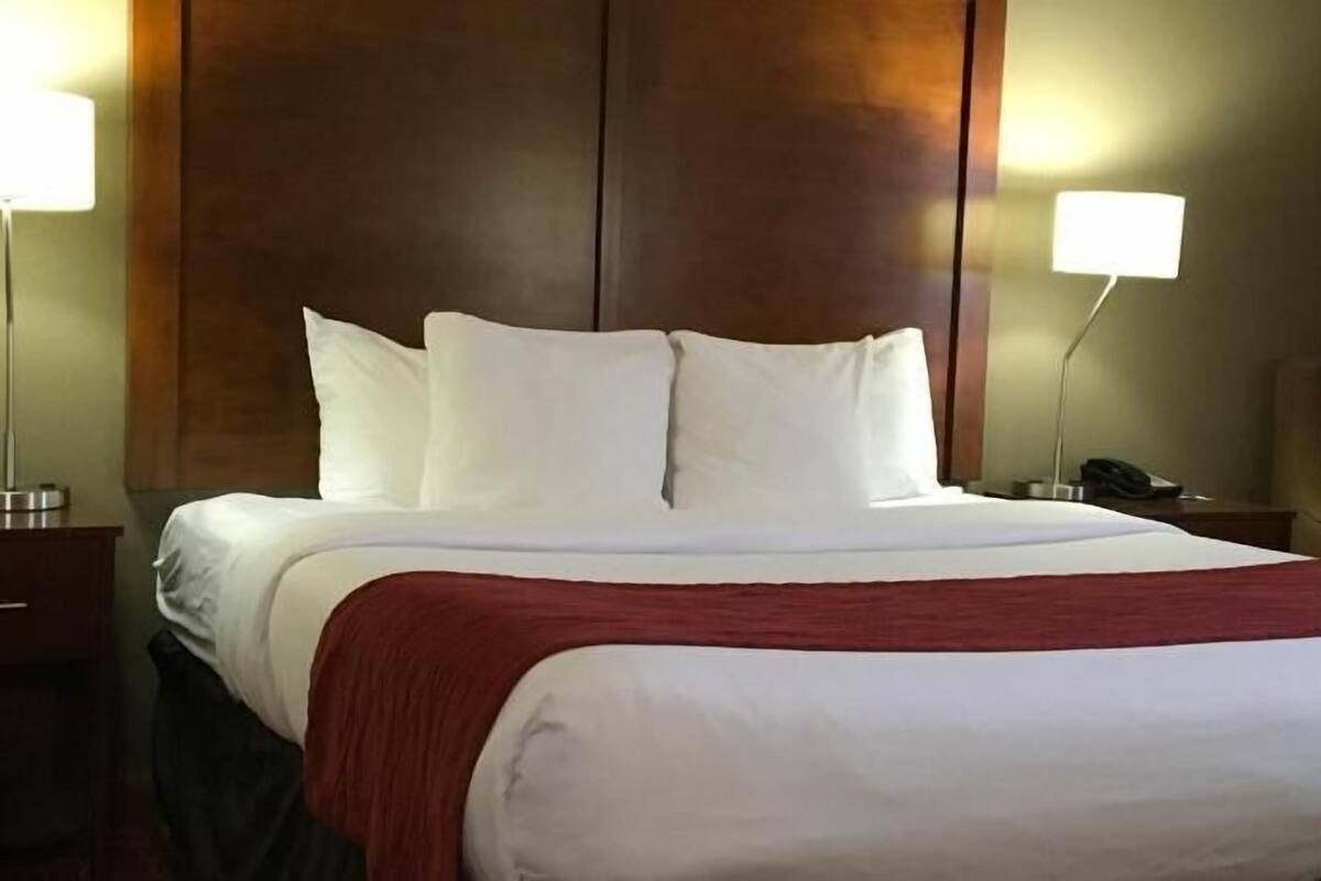 A hotel room with a large bed, two bedside tables, a wooden headboard, and two wall-mounted lamps.