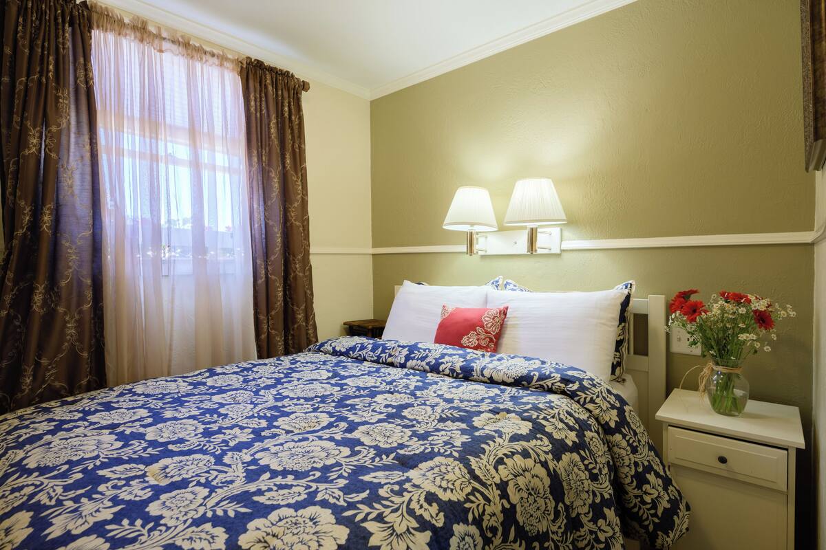 A hotel room with a large bed, two bedside lamps, a nightstand, and a vase with flowers.