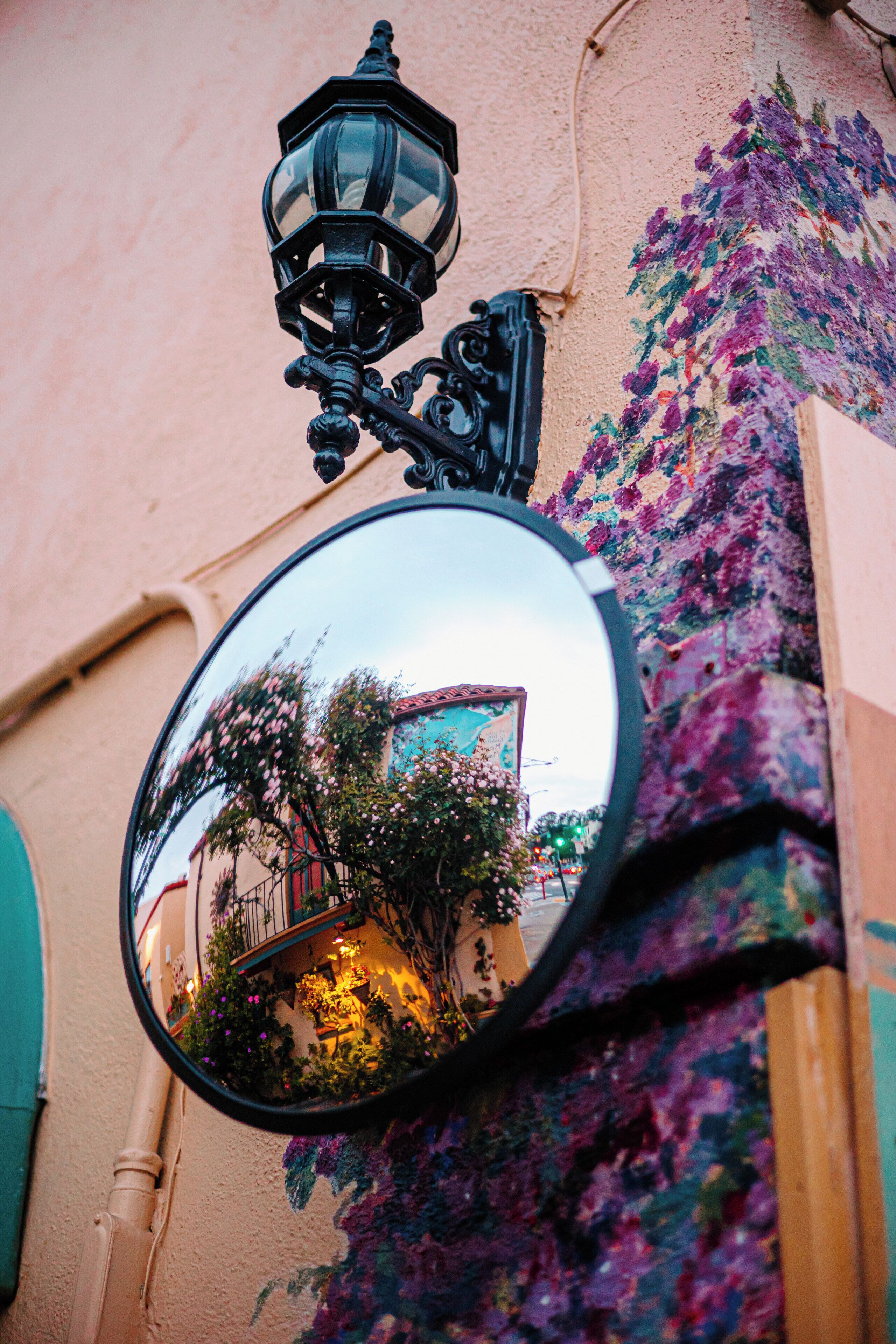 A round mirror reflecting a building with a tiled roof and a balcony.