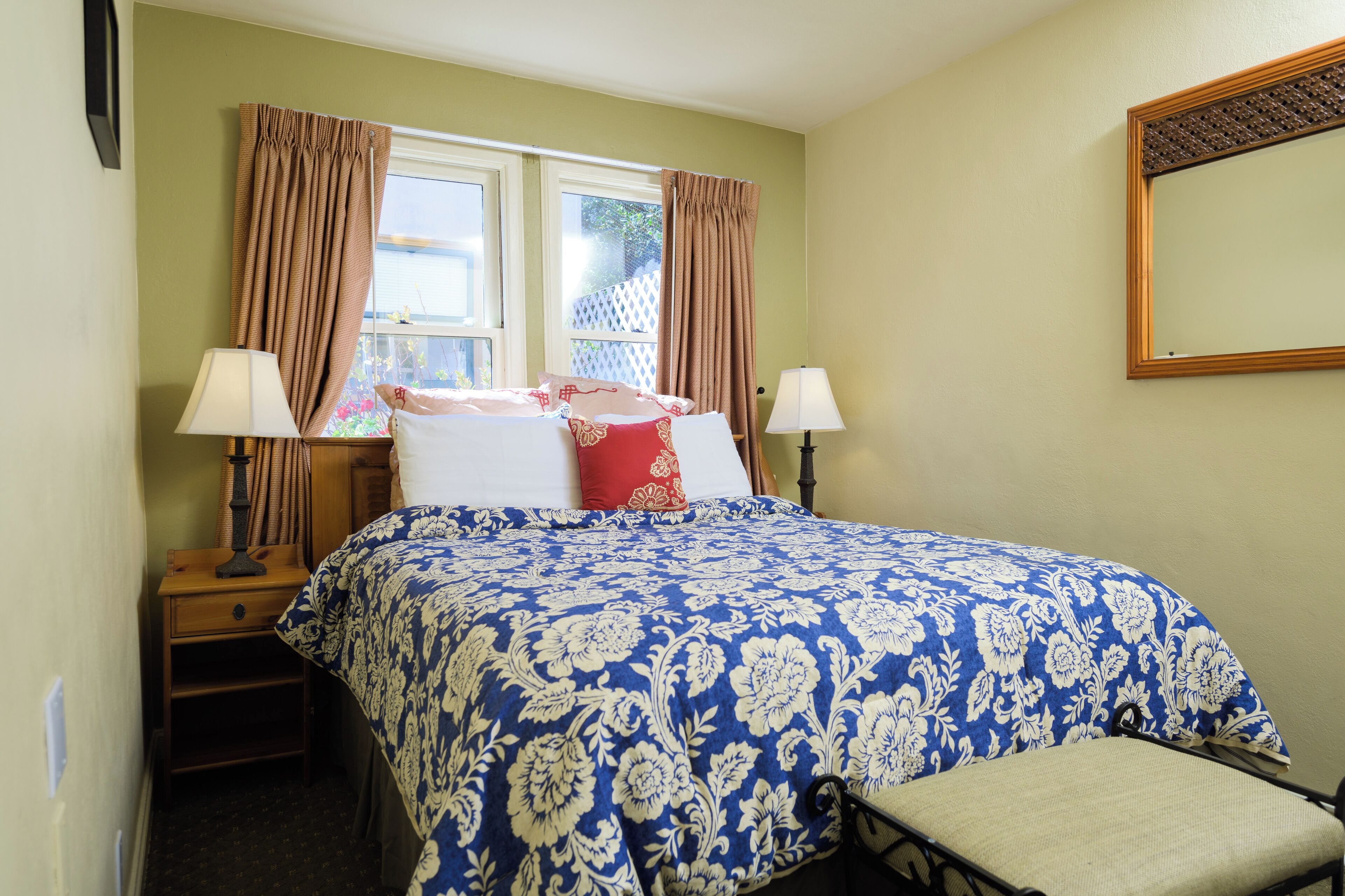 A bedroom with a bed, two bedside tables, two lamps, a chair, and a window with curtains.