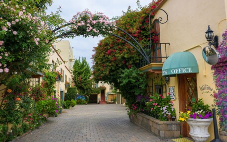 A cobblestone street lined with flower-covered buildings, a welcoming archway, and a sign reading "Office."