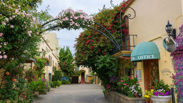 A cobblestone street lined with flower-covered buildings, a welcoming archway, and a sign reading "Office." - Marina Motel (San Francisco)