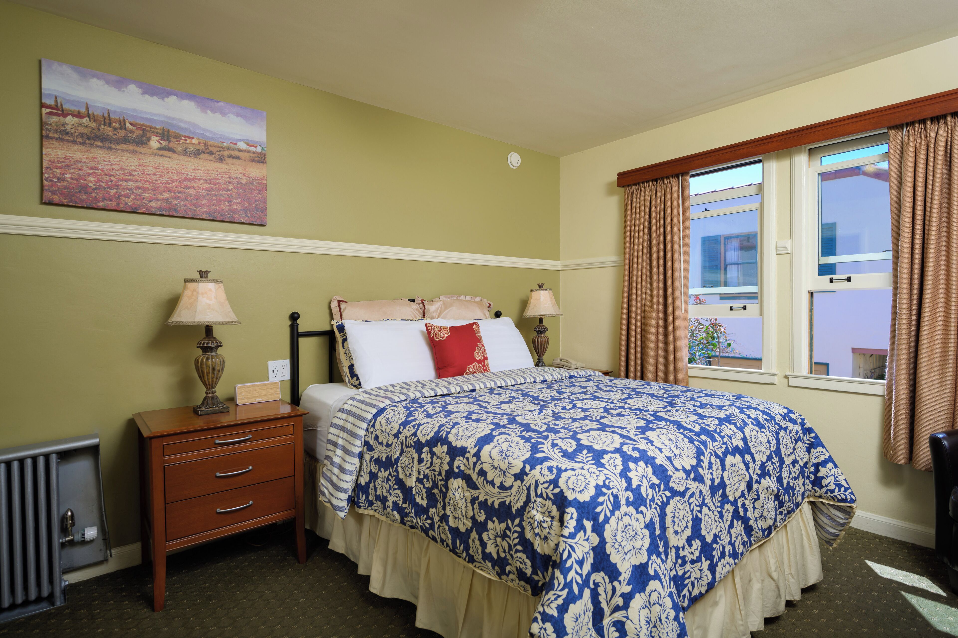A neatly arranged bedroom with a bed, bedside lamps, a nightstand, and a window with curtains.