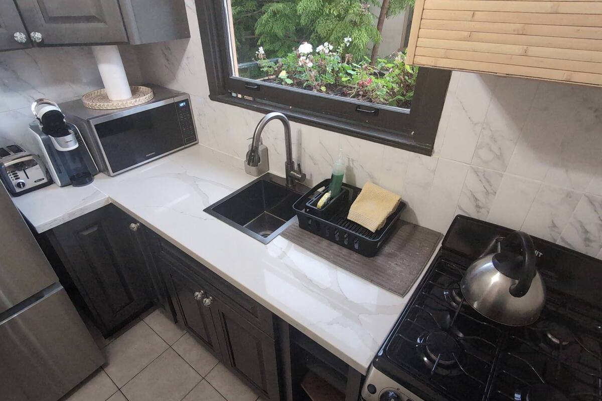 A compact kitchen with a sink, stove, and a window overlooking a garden.