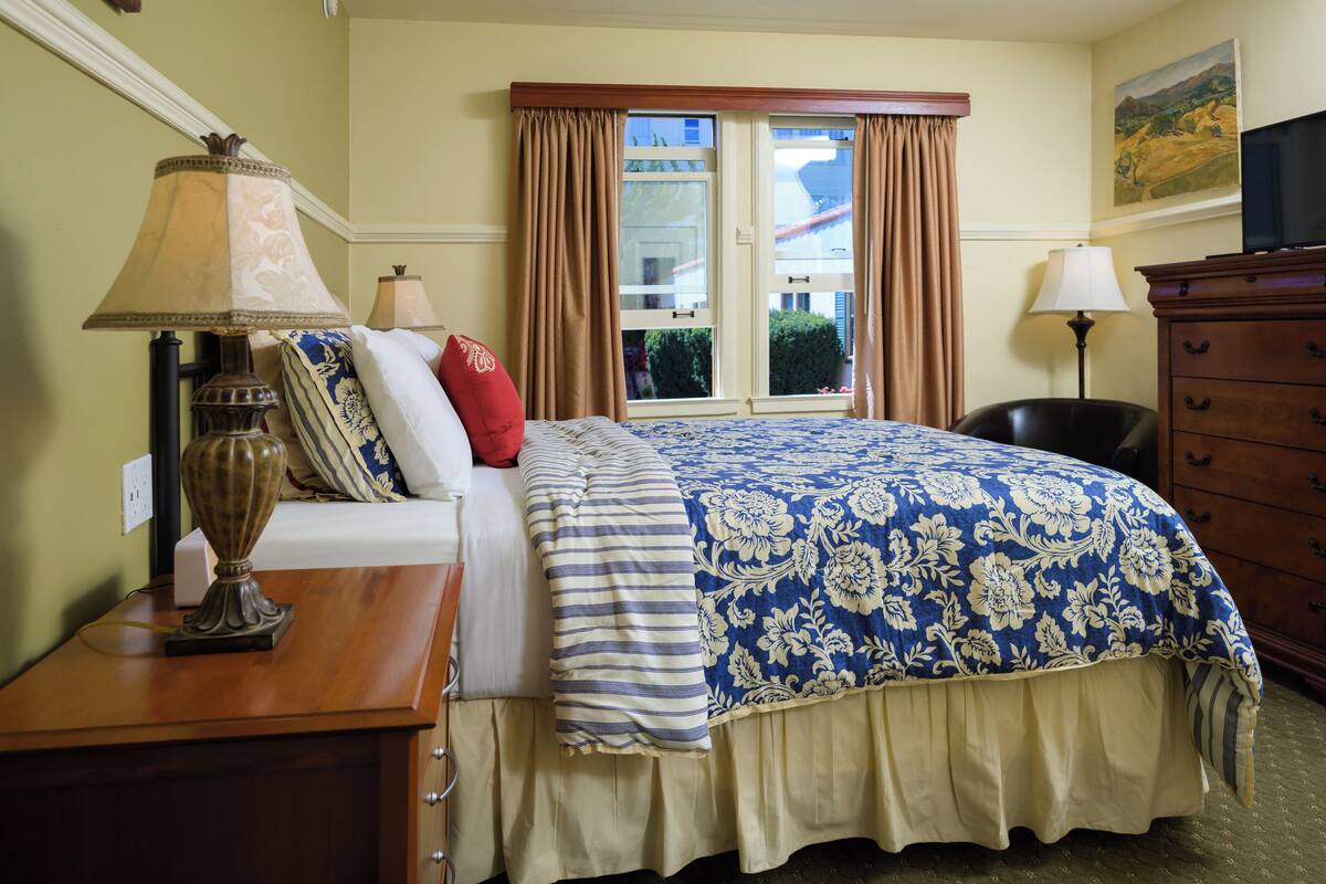 A hotel room with a bed, two bedside lamps, a dresser, and a television.
