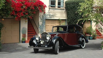 Un coche antiguo estacionado frente a un edificio con puerta de garaje, escalones y plantas en macetas.