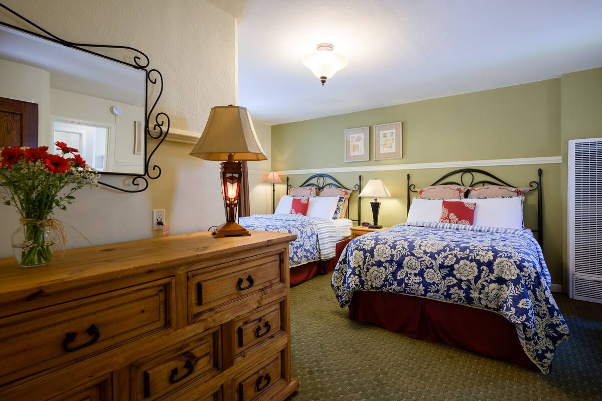 A bedroom with two beds, a dresser, a mirror, and a wall-mounted lamp.