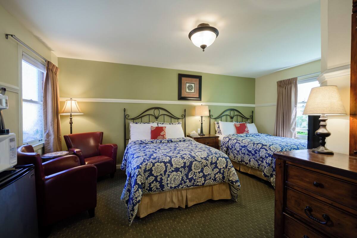 A hotel room with two beds, a desk, a chair, and a dresser.