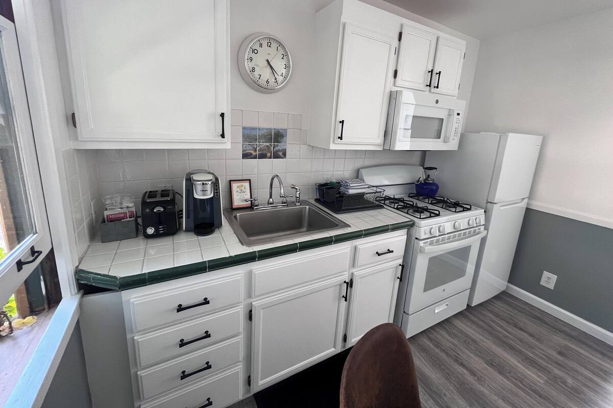 A kitchen with white cabinets, a microwave, a stove, and a sink.