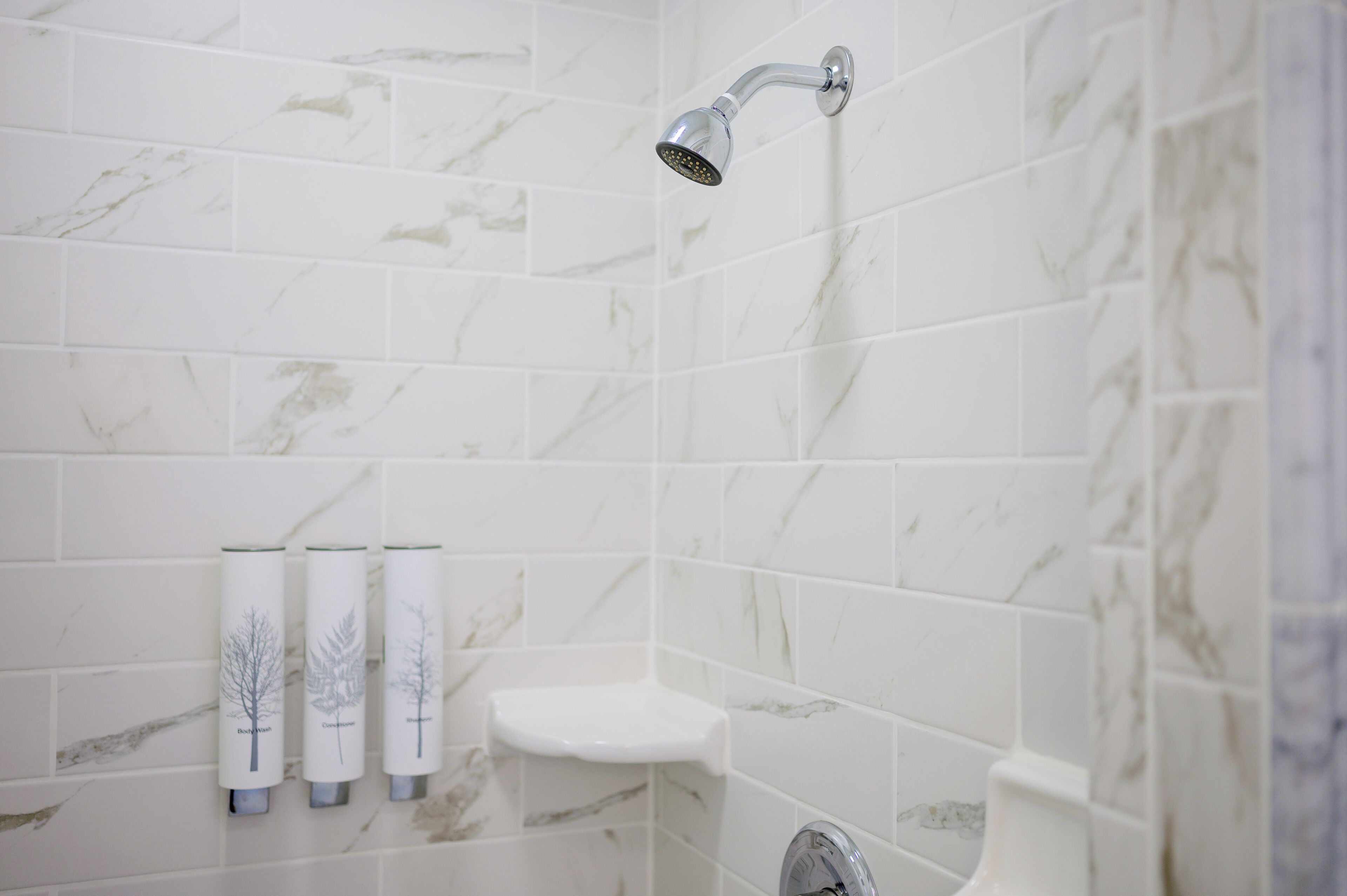 A bathroom with white marble tiles, a showerhead, and three tree-shaped soap dispensers.