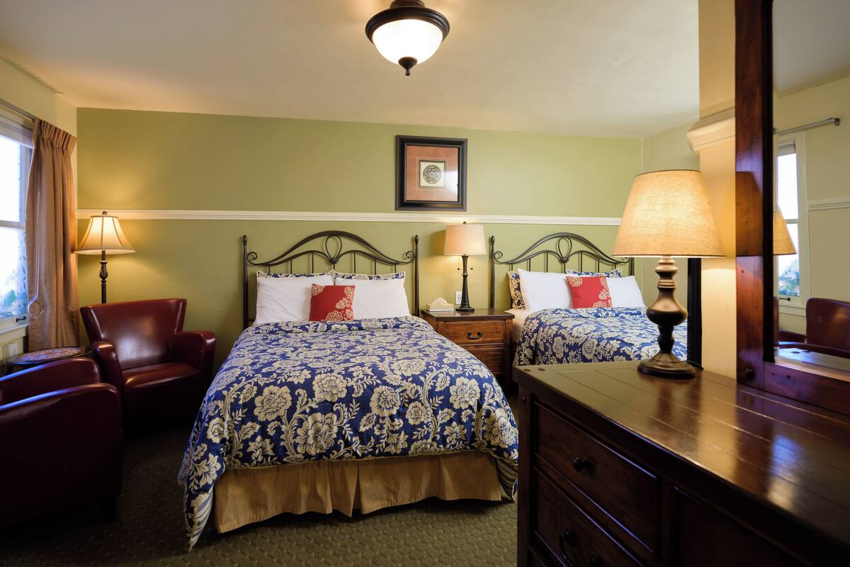 A hotel room with a bed, two bedside tables, a chair, a dresser, and a framed picture on the wall.