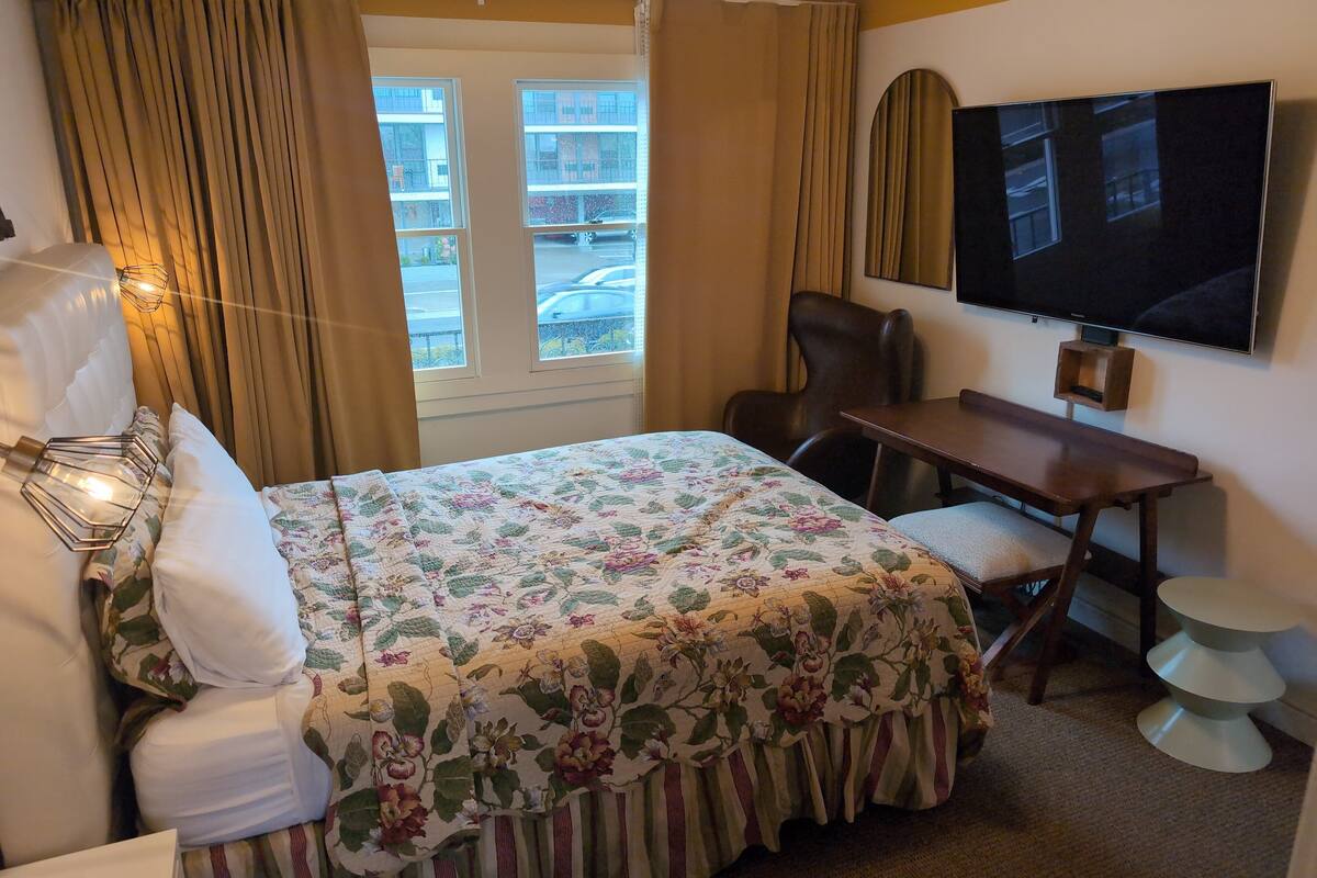 A hotel room with a bed, a desk, a chair, a television, and a window with curtains.
