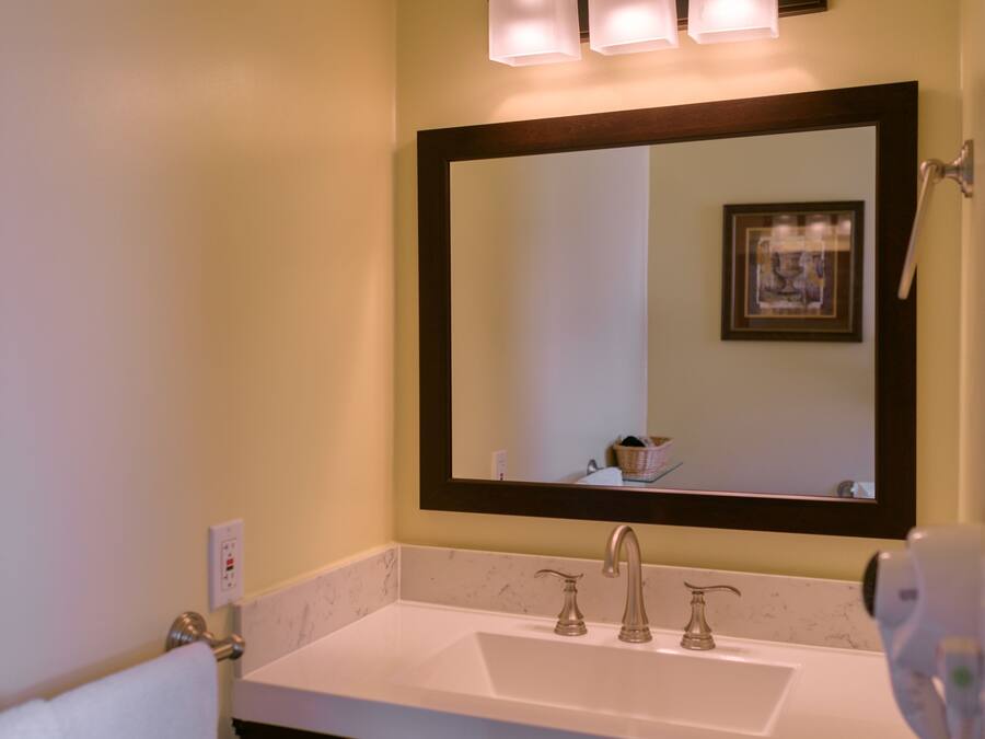 A bathroom with a white sink, dark vanity, and a mirror with three lights.