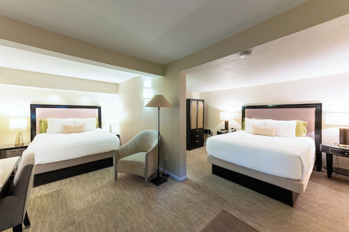A hotel room with two beds, a desk, a chair, and a lamp.