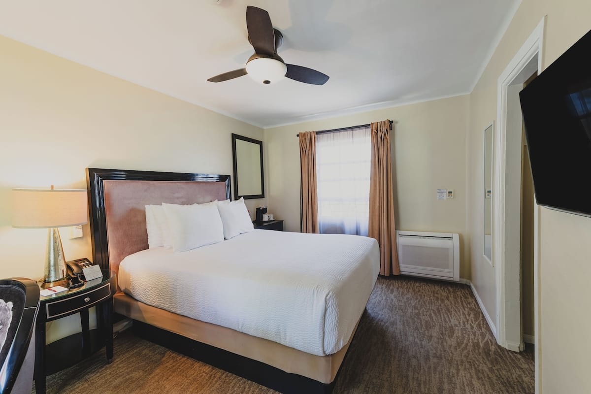 A hotel room with a bed, a ceiling fan, a nightstand with a lamp, and a TV.