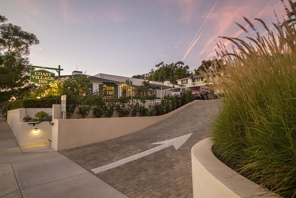 A coastal village inn with a paved driveway leading to the entrance, surrounded by greenery and a clear sky. - Coast Village Inn - Santa Barbara (Santa Barbara)