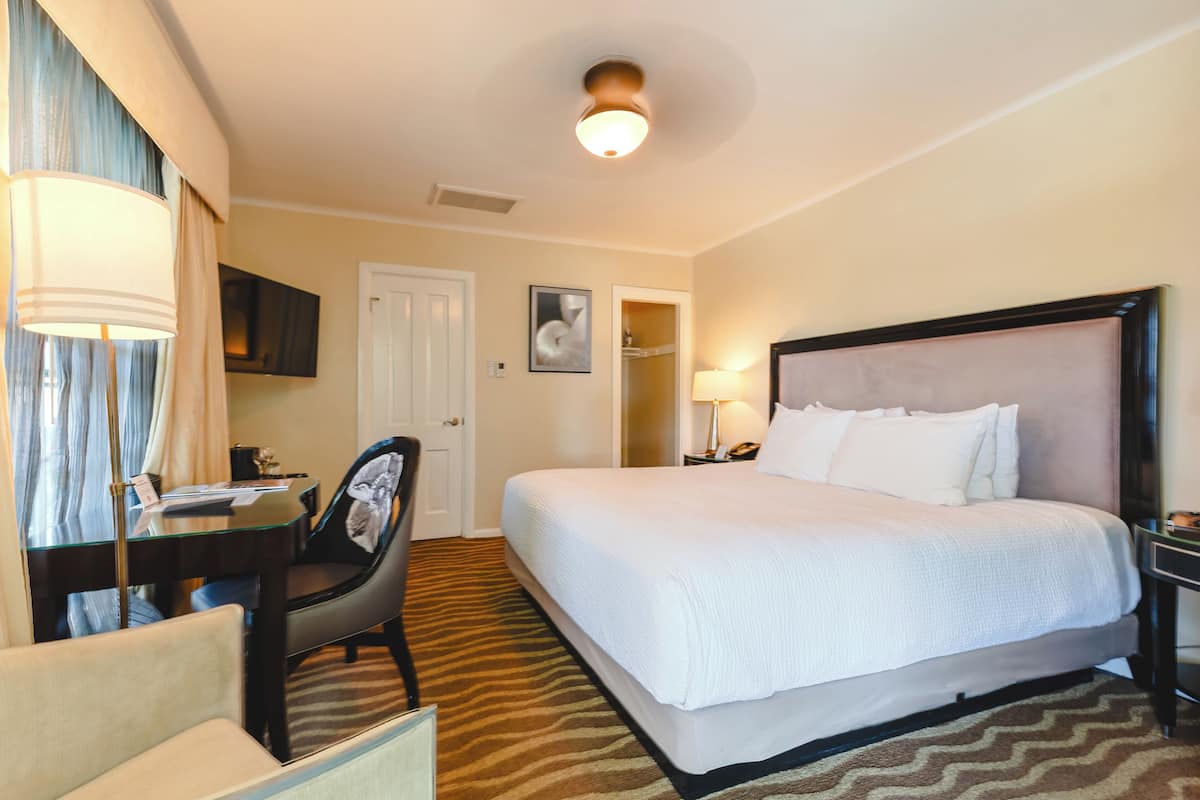 A hotel room with a bed, a desk, a chair, a television, and a door.