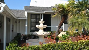 A building with a white exterior, a multi-tiered fountain in the center, and a palm tree to the right. - Coast Village Inn - Santa Barbara (Santa Barbara)