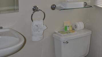 Une salle de bain équipée d’un lavabo, de toilettes et d’une étagère en verre au-dessus des toilettes, où sont rangés les articles de toilette.