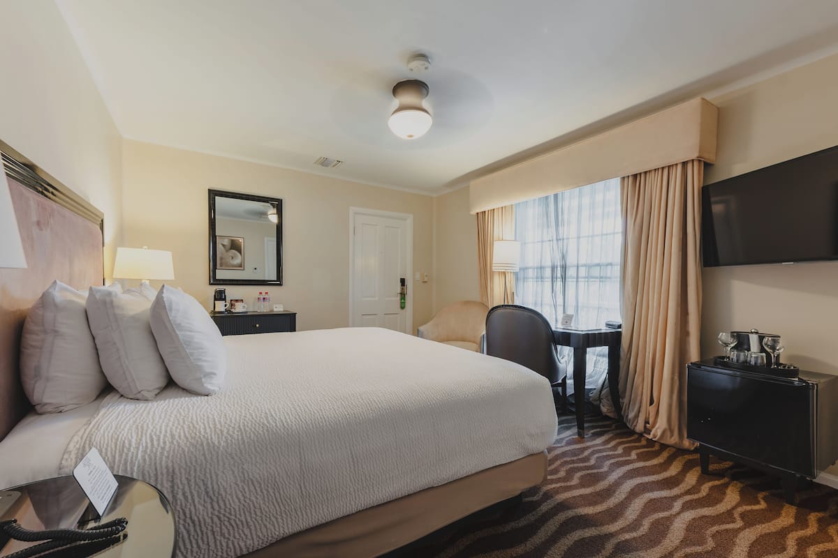 A hotel room with a large bed, a desk, a chair, a television, and a minibar.