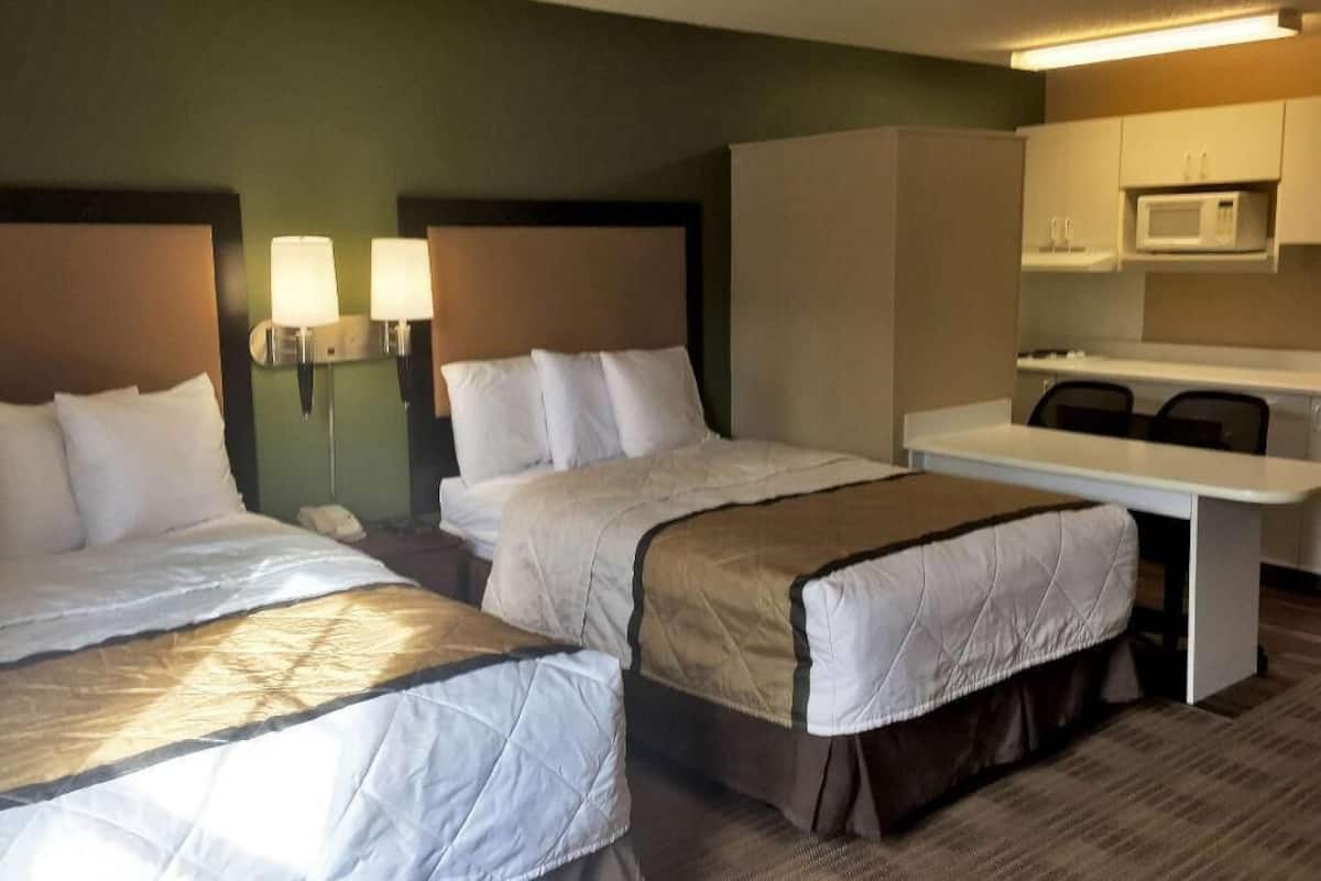 Une chambre d’hôtel avec deux lits, un bureau, un four à micro-ondes et une petite kitchenette.
