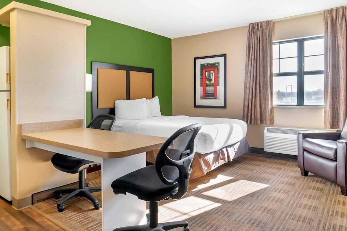 Une chambre d’hôtel avec un lit, un bureau, une chaise et une fenêtre avec des rideaux.