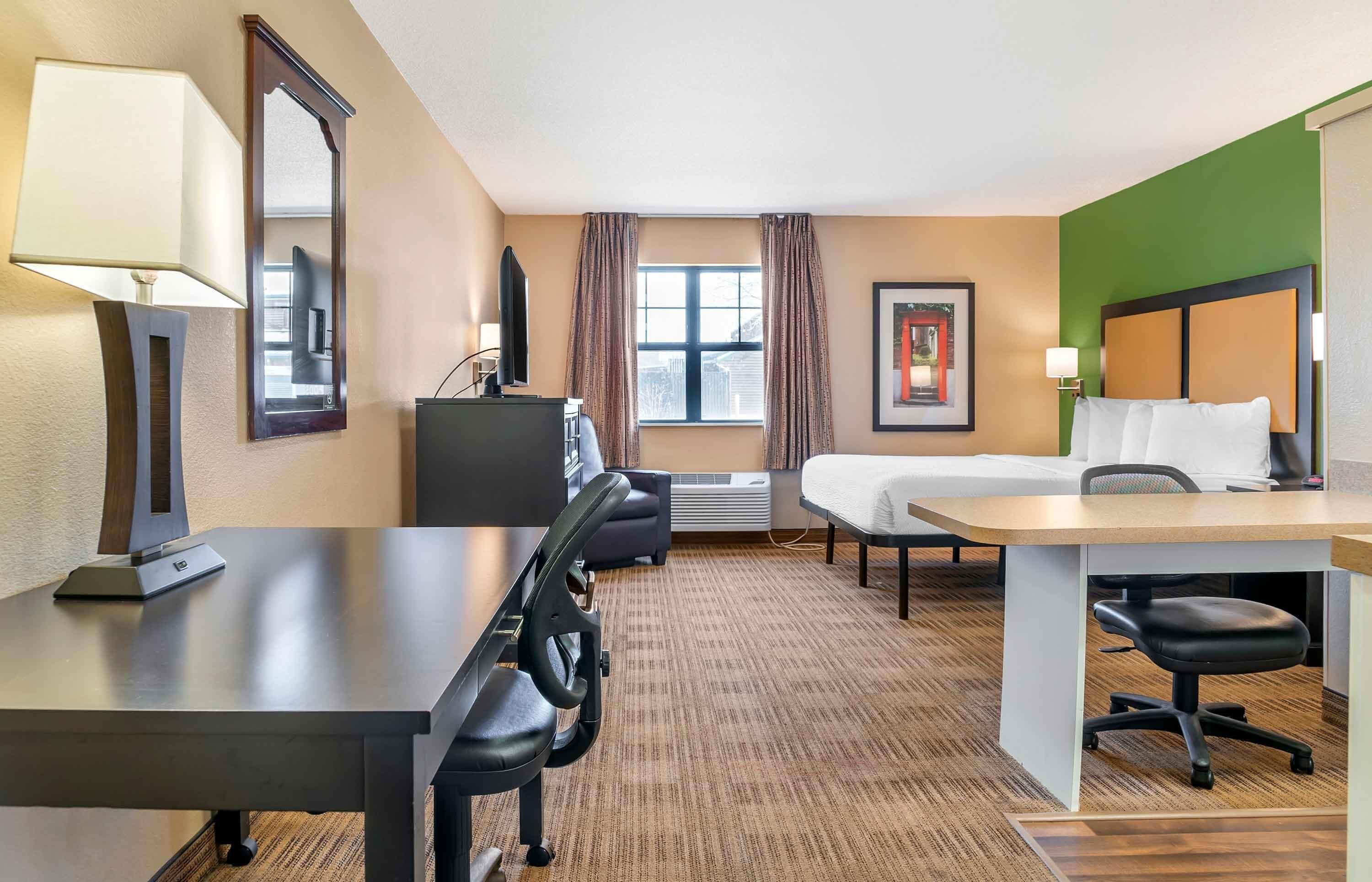 Una habitación de hotel con escritorio, silla, cama y un espejo grande.